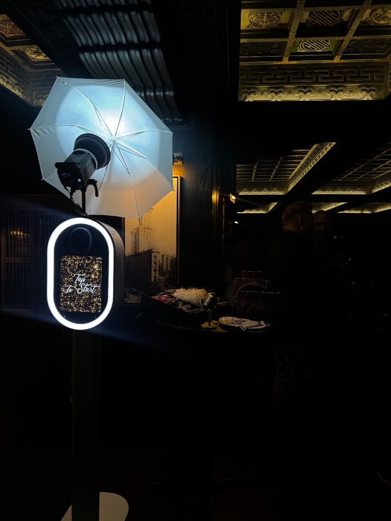 Photo booth with Tap to Start screen and studio umbrella in dimly lit venue with ornate ceiling and props